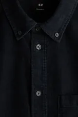 Camisa de pana de algodón suave color negro, con cuello americano, bolsillo superior en el pecho y cierre frontal de botones.