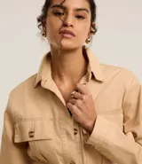 Campera trench coat color beige, con cuello inglés, manga larga, abotonado delantero, bolsillos con solapa y lazo en la cintura.