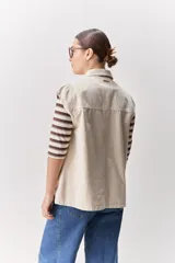 Chaleco de algodón color beige, de calce relajado, con cuello clásico, hombros amplios, cierre frontal con broches metálicos y bolsillos delanteros con solapa.