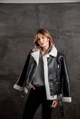 Campera tipo gamulán de eco cuero negro con interior y solapas de corderito sintético en color crudo. Presenta cierre frontal, bolsillos laterales con cierre y cinturón ajustable en la cintura.