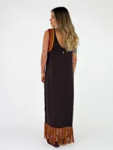 Vestido largo negro de punto con tirantes anchos rayados en tonos marrones y amarillos, escote redondo y flecos multicolor en el ruedo.