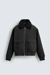 Cazadora bomber de corte cropped confeccionada en algodón, color negro. Presenta cuello de solapa con efecto borreguillo a contraste, cierre frontal con cremallera metálica, bolsillos delanteros tipo plastrón con solapa y acabados en rib en puños y bajo.