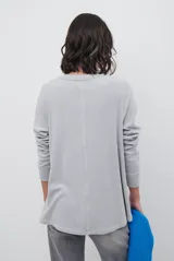 Remera de manga larga en color beige, confeccionada en tejido de punto con costuras a la vista en contraste. Presenta un corte holgado, cuello redondo y un pequeño bordado distintivo en la parte inferior.