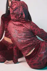 Conjunto de buzo y pantalón de terciopelo rojo con estampado animal print negro. El buzo es de corte ajustado, con capucha y cierre frontal. El pantalón es de corte acampanado y tiene un aplique de estrella de strass en la parte trasera.