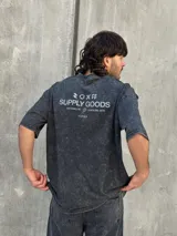 Remera gris con efecto gastado, corte oversize, mangas cortas y estampado en la espalda con el texto "SUPPLY GOODS DESIGNED IN PUNTA DEL ESTE".