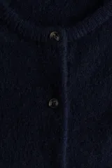 Saco de punto suave con lana, de corte holgado y diseño minimalista. Presenta cuello redondo, cierre frontal con botones y hombros levemente caídos. Posee terminaciones acanaladas en cuello, puños y bajo.