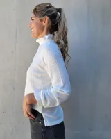 Polera de manga larga en tejido acanalado color blanco, con cuello alto y puños con detalle de punto smock fruncido.