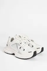 Zapatillas urbanas de suela alta, con diseño multicapa que combina malla y paneles sintéticos en tonos blanco y crema, con pequeños detalles en negro.