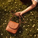 Mini cartera bandolera de cuero, de formato compacto y diseño atemporal con solapa frontal y costuras artesanales decorativas en el borde. Cuenta con el logotipo de la marca grabado en la parte delantera y correa larga regulable.