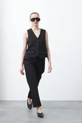 Chaleco sastrero negro con escote en V, cierre frontal de botones marrones, sin mangas y con pinzas de entalle.