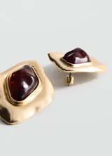Aros de diseño irregular con estructura de metal dorado y aplique central de resina en tono rojizo. Cierre metálico a presión.