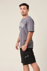 Bermuda deportiva color verde militar, de corte suelto, con cintura elástica y cordón de ajuste. Cuenta con detalles de líneas verticales en los costados y bolsillos laterales con cierre.