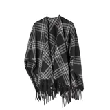 Poncho abierto con diseño de cuadros escoceses en tonos negro, gris y blanco. Presenta bordes con flecos largos y una caída fluida sobre los hombros.
