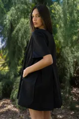 Vestido corto de algodón color negro, con mangas cortas, cuello redondo y diseño con tablas frontales y traseras que le otorgan una caída holgada.