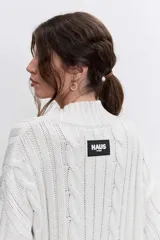 Sweater de punto con diseño de trenzas, cuello alto y mangas largas con puños acampanados. Presenta un corte holgado con terminación asimétrica en el ruedo.