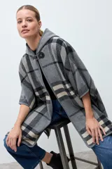 Capa abierta con capucha, diseño a cuadros en tonos grises, negros y beige. Presenta un cierre frontal tipo hebilla de cuero sintético en el cuello y mangas cortas tipo kimono.
