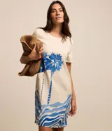 Vestido corto de viscolino color marfil con escote redondo, mangas cortas y bolsillos laterales. Cuenta con un estampado frontal en tonos de azul que representa un paisaje de palmeras y olas del mar.
