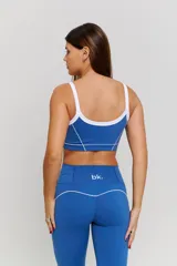 Conjunto deportivo compuesto por un top y un pantalón largo. El top es de estilo deportivo con breteles finos, escote redondo y detalle de ribete blanco en contraste, con el logo 'bk.' estampado en el frente. El pantalón es de tiro alto, ajustado en la cintura y caderas, con diseño acampanado en la parte inferior.