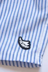 Short de baño celeste con rayas verticales blancas, cintura elástica con cordón ajustable, bolsillos laterales y trasero con cierre, logo de la marca bordado en la pierna.