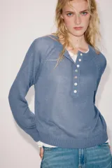 Sweater de punto color beige con cuello redondo, manga larga y cierre frontal parcial con botones. Presenta terminaciones en rib en cuello, puños y dobladillo.