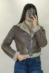 Campera tipo aviador de cuero sintético negro con interior y detalles de piel sintética al tono en cuello, puños y ruedo. Presenta cierre frontal cruzado y cinturón ajustable con hebilla metálica en la cintura.