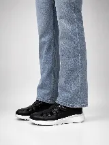 Zapato cerrado tipo zapatilla de cuero natural negro, combinando sectores lisos y texturados, con aperturas laterales y cierre de velcro. Cuenta con suela blanca liviana y anatómica.