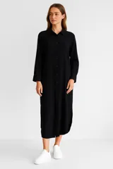 Túnica negra de lino, corte holgado, con cuello camisero, manga larga y cierre frontal con botones.