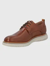 Zapato de vestir Hush Puppies modelo Rustic, confeccionado en cuero color marrón con cordones al tono. Presenta una suela de EVA en color gris claro con detalle de marca FLX en el lateral.