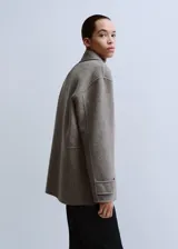 Chaqueta estilo overshirt de paño color gris, con cuello solapa, cierre frontal de botones oscuros, bolsillos con solapa en el pecho y bolsillos aplicados en la parte inferior.