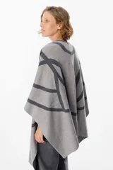 Ruana de tejido de punto con diseño geométrico de líneas curvas en tonos beige y visón. Presenta una caída fluida y envolvente, ideal para usar como capa sobre otras prendas.