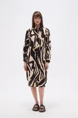 Vestido camisero de corte holgado con estampado abstracto en tonos negro y beige. Presenta cuello camisero, cierre frontal completo con botones y mangas largas con puños.