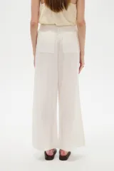 Pantalón de lino blanco, de corte ancho y tiro alto con cintura elástica fruncida y cordón ajustable.