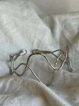 Brazalete rígido plateado con diseño irregular de ondas.
