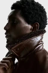 Campera de estilo aviador confeccionada en tejido revestido con acabado de cuero sintético. Presenta cuello de sherpa en contraste, cierre frontal de cremallera, hombros caídos y bolsillos delanteros de parche con solapa y botón a presión. Incluye elástico fruncido en el bajo y puños ajustables con botón a presión.