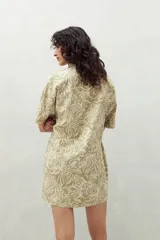 Vestido camisero corto color verde claro con estampado de hojas en blanco. Tiene cuello camisero, cierre frontal con botones y corte recto.