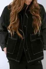 Campera color caramelo con mangas de denim azul oscuro. Presenta cuello alto, cierre frontal con botones, cuatro bolsillos delanteros con solapa y pespuntes blancos decorativos.