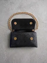 Riñonera negra de diseño acolchado con textura trenzada, cuenta con una cadena decorativa gruesa en color dorado y cierre de solapa.