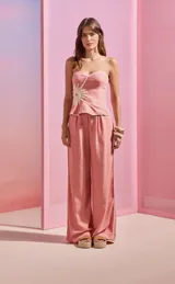 Pantalón de lino rosado de silueta amplia y fluida con detalle de hebilla metálica en forma de sol en la cintura. Su diseño de tiro alto con pliegues frontales estiliza la figura, mientras que las aberturas laterales con bordado contrastante añaden un toque sofisticado y veraniego.