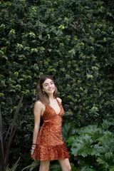 Vestido corto negro con estampado de plumas doradas, escote en V, breteles finos cruzados en la espalda, cut-outs laterales y volado en el ruedo.