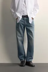 Jeans regular fit de mezclilla negra con efecto lavado, corte recto y tiro medio. Cuenta con diseño de cinco bolsillos y cierre frontal con cremallera y botón.