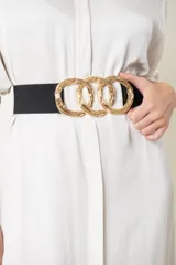 Cinto elástico color beige con hebilla dorada formada por tres aros entrelazados.