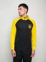 Buzo deportivo de entrenamiento, color negro en el torso y amarillo en las mangas y cuello. Es de manga larga, con cuello alto y cierre parcial frontal. Presenta un escudo con estrellas en el pecho.