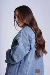 Campera clásica de jean celeste con cuello camisero, bolsillos frontales con solapa y cierre con botones metálicos. Presenta detalles de pequeños brillos blancos dispersos en la parte delantera y las mangas.