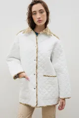 Campera capitoneada de color blanco con diseño acolchado en forma de rombos. Presenta detalles en tela a cuadros en el cuello, los bordes frontales, los bolsillos y el ruedo. Posee cierre frontal con botones metálicos y un corte holgado.