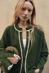 Chaqueta de punto color verde oscuro con cuello redondo y cierre frontal de botones. Presenta detalles de vivos en color crema en el cuello, la tapeta de botones y los puños.