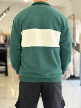 Hoodie de corte clásico con medio cierre y cuello alto, en color marrón con una franja horizontal blanca en el pecho que incluye el logo estampado en negro. Presenta además un pequeño bordado en el hombro izquierdo y puños y cintura elastizados de rib.
