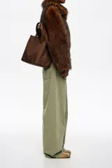 Bolso tipo tote de Bimba y Lola en color marrón, confeccionado en gabardina con detalles en piel. Cuenta con doble asa de mano, asa bandolera regulable, cierre con botón de presión y logo metálico aplicado en el frente.