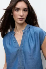 Blusa de lyocell en tono azul medio, con mangas cortas, escote en V y detalles de pespuntes decorativos en la parte frontal.