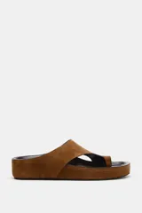 Sandalia plana tipo chinela confeccionada en serraje color marrón, con diseño de pala ancha y separador para el dedo. Cuenta con suela de plataforma baja y punta redonda.