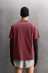 Camiseta de entrenamiento de ajuste relajado, color vino tinto, confeccionada en tejido de peso medio con mezcla de algodón. Presenta cuello redondo con acabado en vivo doble y manga corta.